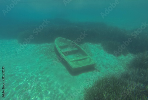 An old rowing boat is abandoned on the sandy bottom under the water.