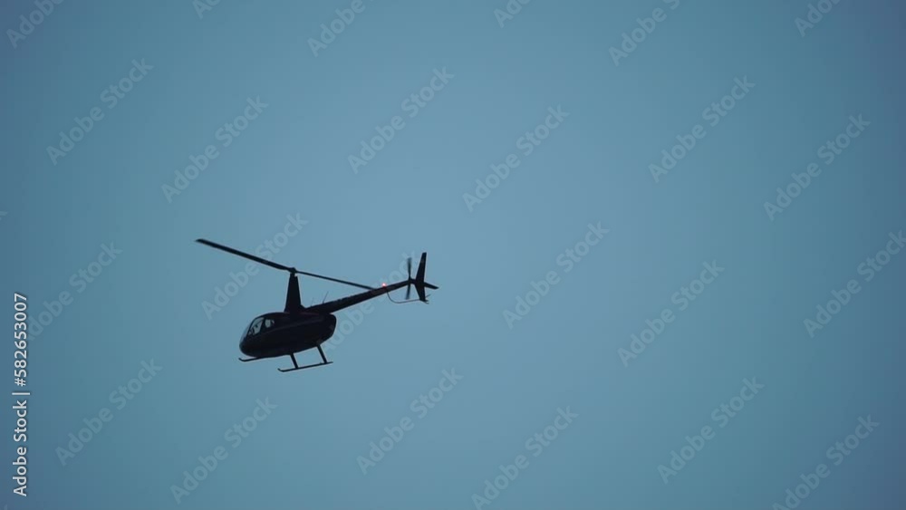 Modern helicopter fly in sky, as viewed from the ground. Silhouette of a modern helicopter hovering in the sky, the blades spin slowly. Slow motion Modern helicopter fly in sky, as viewed from the ground. Silhouette of a modern helicopter hovering in the sky, the blades spin slowly. Slow motion