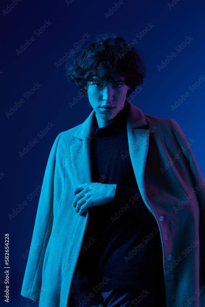 Man fashion in coat on dark blue background, neon light, style and trends, mixed light, men's fashion, copy place