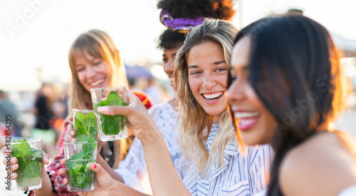 A group of girls of different nationalities having fun at a beach party drinking mojitos and dancing.