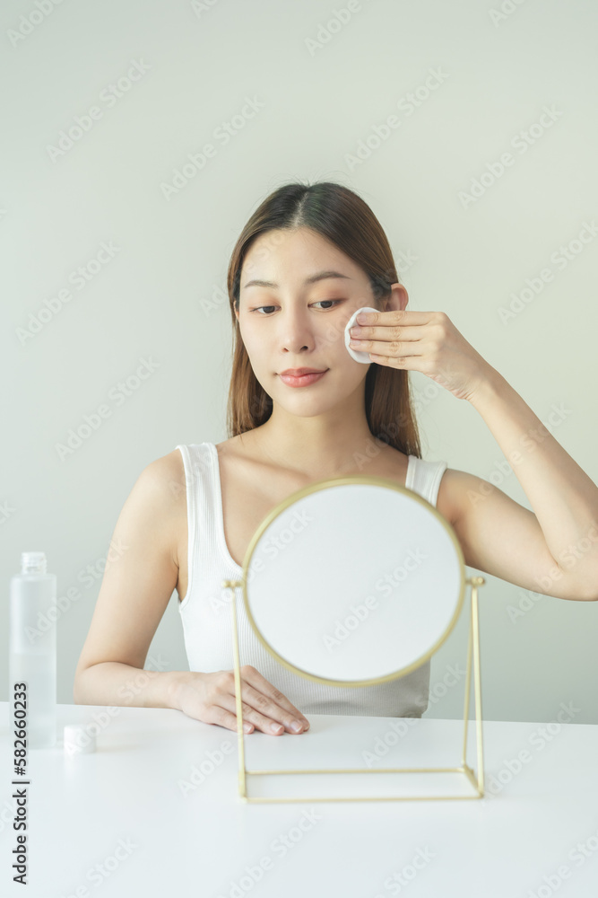 Happy beauty, attractive asian young woman, girl looking reflect in mirror, hand holding cotton pad, applying facial wipe on her face remover makeup, essence or lotion for treatment, skin care routine Happy beauty, attractive asian young woman, girl looking reflect in mirror, hand holding cotton pad, applying facial wipe on her face remover makeup, essence or lotion for treatment, skin care routine