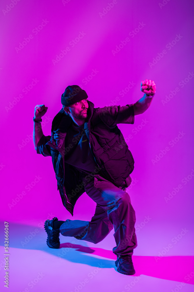 Fashionable professional dancer man in stylish urban clothes dancing in a creative color studio with pink and neon lights