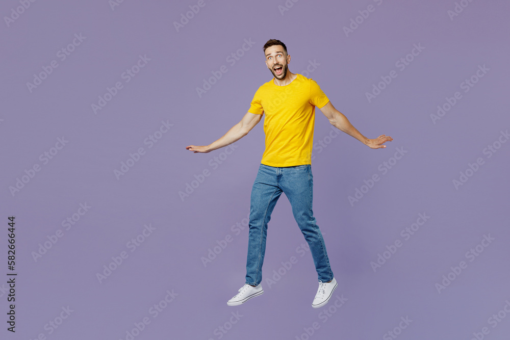 Full body young excited surprised caucasian man wear yellow t-shirt jump high with outstretched hands look camera isolated on plain pastel light purple background studio portrait. Lifestyle concept.