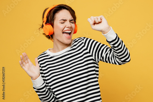 Foto Young vivid woman wear casual striped black and white shirt headphones listen to music in headphones dance have fun sing song in microphone isolated on plain yellow color background studio portrait