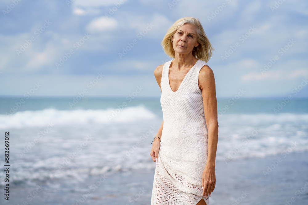 Mature woman walking on the beach. Elderly female standing at a seaside location