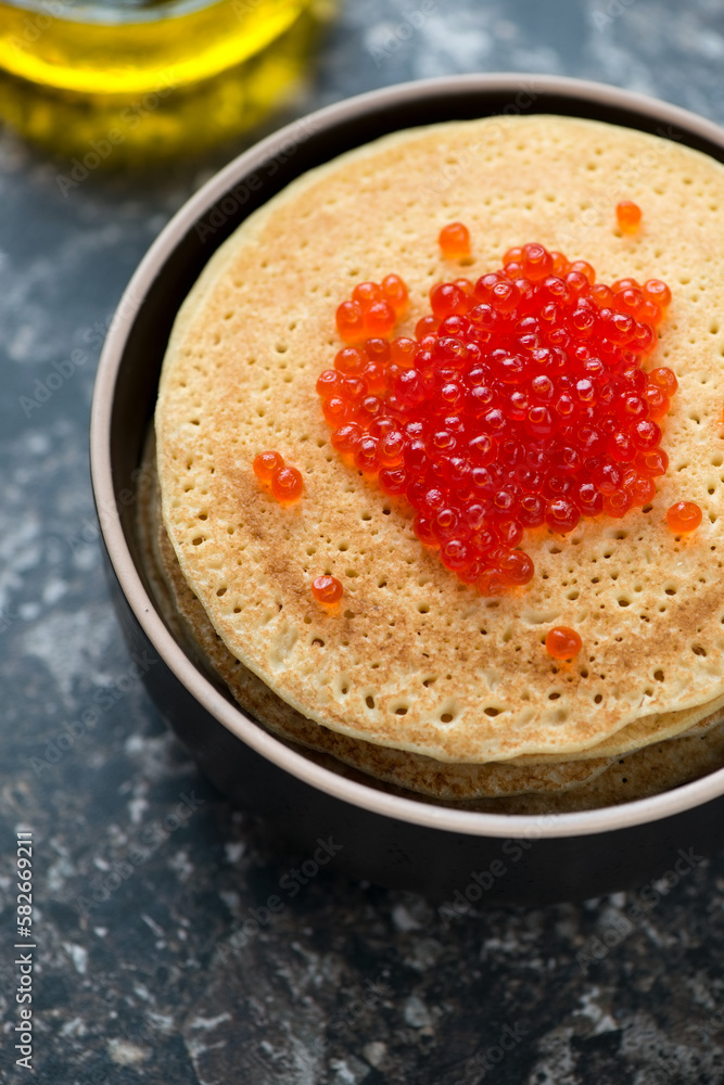 Bowl of pancakes topped with red caviar, vertical shot on a dark-brown granite background, close-up Bowl of pancakes topped with red caviar, vertical shot on a dark-brown granite background, close-up