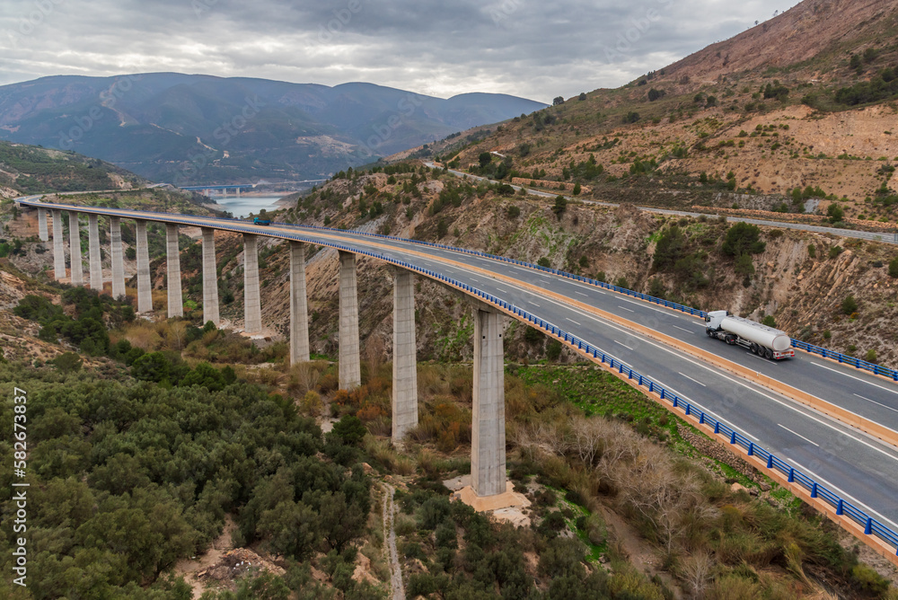 Landscape with a very long and high viaduct in the foreground that surrounds a reservoir, and where a fuel tanker truck circulates, top view. Landscape with a very long and high viaduct in the foreground that surrounds a reservoir, and where a fuel tanker truck circulates, top view.