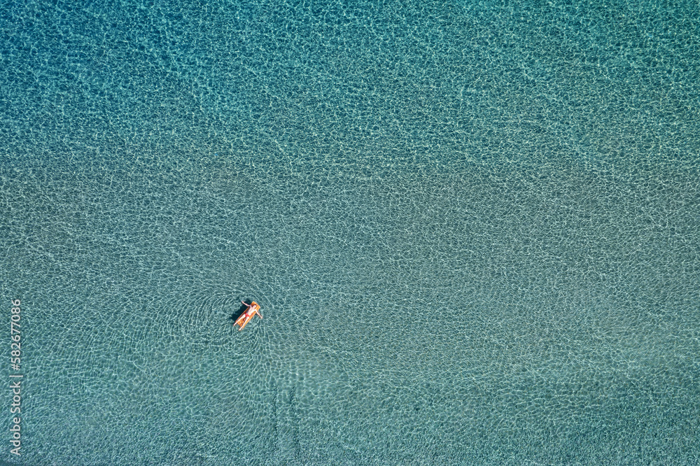 Aerial top down view of a man on the inflatable mattress on clear sea water