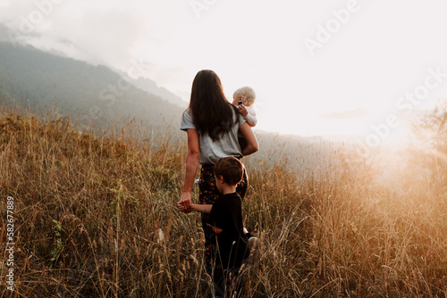 Slika na platnu mother with children from behind, walk across a field among the mountains in the beautiful sunset light on a summer day