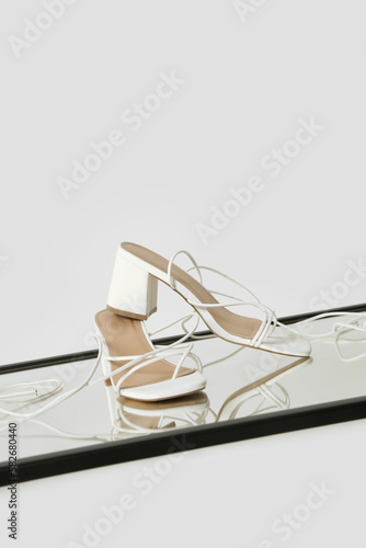 Creative studio shot of white strappy lace up block heel sandals, product photography photo