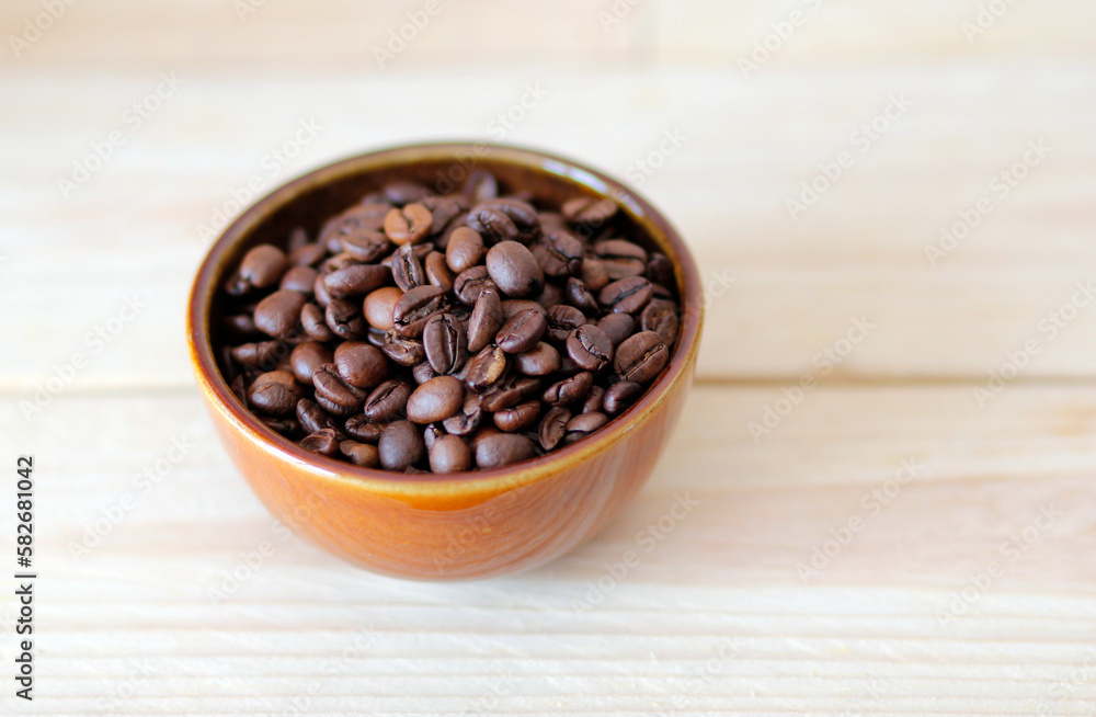 Fototapeta premium close-up of brown coffee beans in a bowl, coffee beans background, coffee beans in a bowl on wooden table, space for text, roasted coffee beans