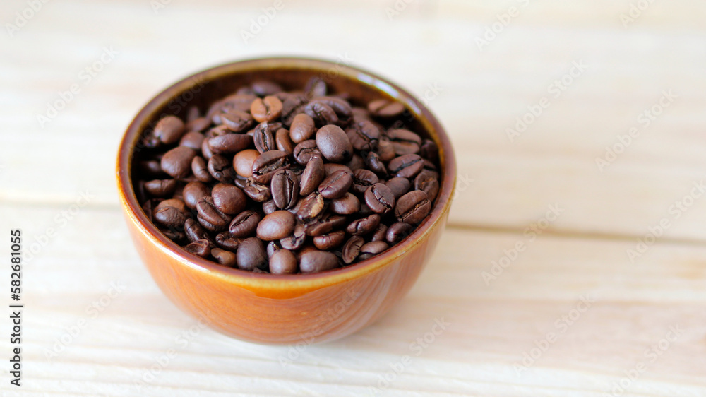 Fototapeta premium close-up of brown coffee beans in a bowl, coffee beans background, coffee beans in a bowl on wooden table, space for text, roasted coffee beans