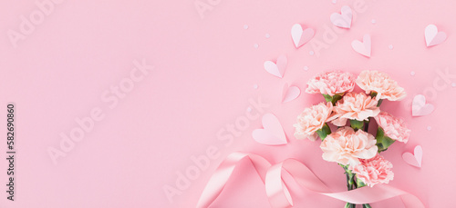 Pink carnation flowers and paper hearts on pastel background for Mothers day card. © juliasudnitskaya