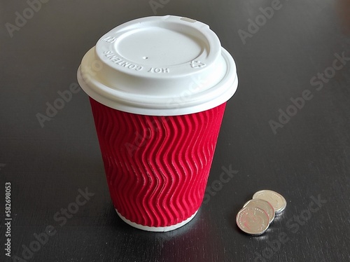 Red paper disposable cup with a lid, coins on a black background