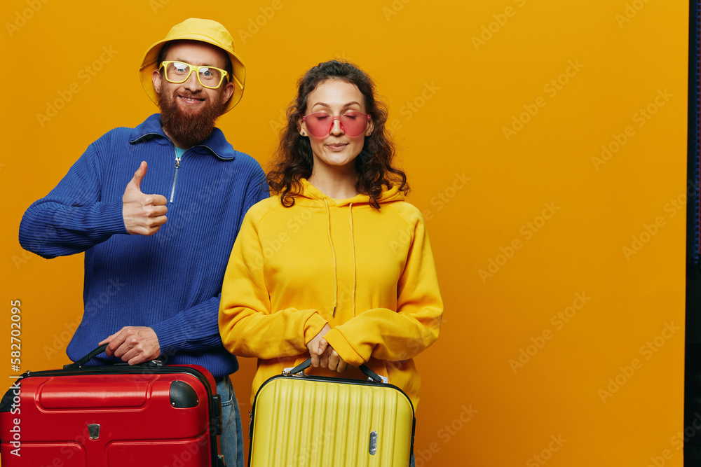 Woman and man smiling, suitcases in hand with yellow and red suitcase smiling merrily and crooked, yellow background, going on a trip, family vacation trip, newlyweds. Woman and man smiling, suitcases in hand with yellow and red suitcase smiling merrily and crooked, yellow background, going on a trip, family vacation trip, newlyweds.