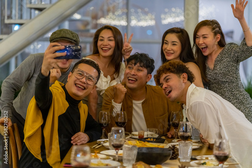 Group of Asian people using mobile phone taking selfie together during outdoor celebration dinner party in the garden on summer holiday vacation. Man and woman friend reunion meeting at restaurant.