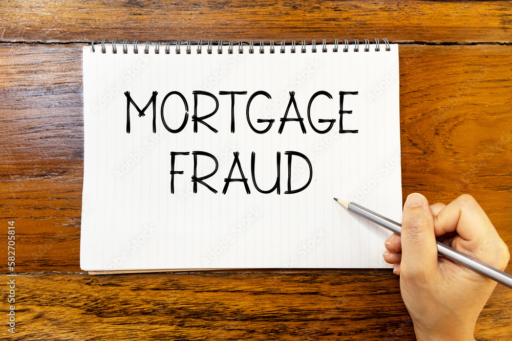 Mortgage fraud handwriting text on blank notebook paper on wooden table with hand holding pencil. Business concept and legal concept about mortgage fraud. Mortgage fraud handwriting text on blank notebook paper on wooden table with hand holding pencil. Business concept and legal concept about mortgage fraud.