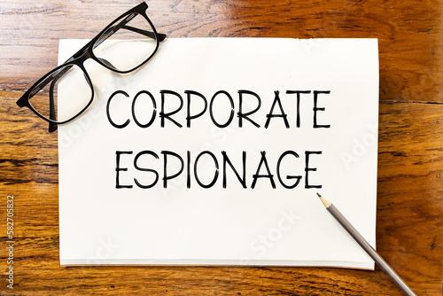 Canvas Print Corporate espionage text on blank notebook paper on wooden table with pencil and glasses aside
