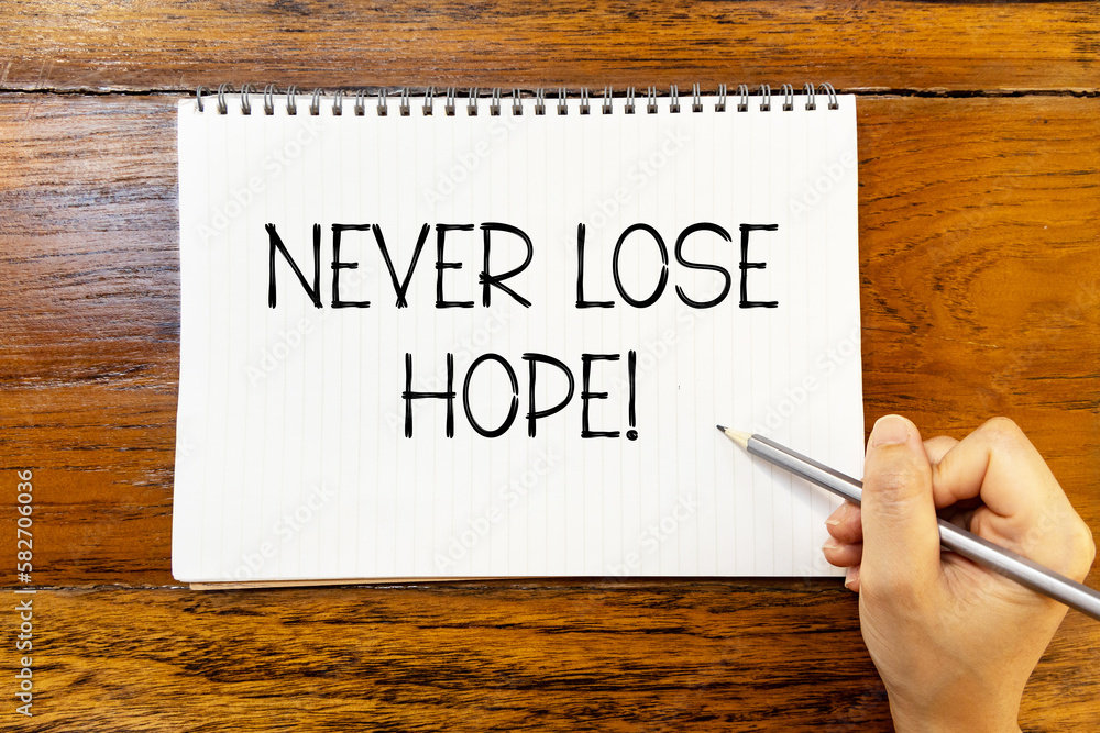 Never lose hope handwriting text on blank notebook paper on wooden table with hand holding pencil. Business concept about don't give up. Never lose hope handwriting text on blank notebook paper on wooden table with hand holding pencil. Business concept about don't give up.