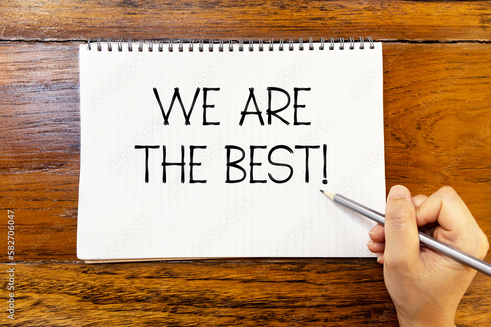 We are the best handwriting text on blank notebook paper on wooden table with hand holding pencil. Business concept to inform audience that we are the best. We are the best handwriting text on blank notebook paper on wooden table with hand holding pencil. Business concept to inform audience that we are the best.