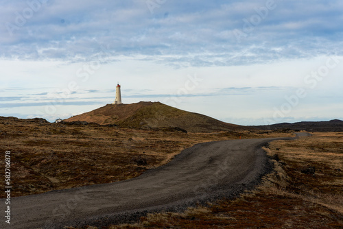 route sinueuse emenent vers un phare blanc et rouge d’Islande se trouvant au sommet d'une montage volcanique 