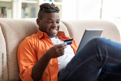 Cheerful young black man using digital pad and bank card