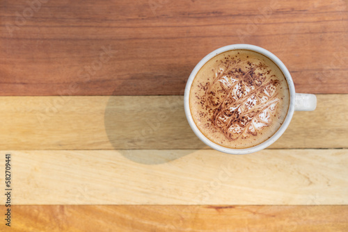 top view of hot late-art coffee in a white ceramic cup on wooden table background, hot cholate or cocoa with milk foam low caffeine beverage