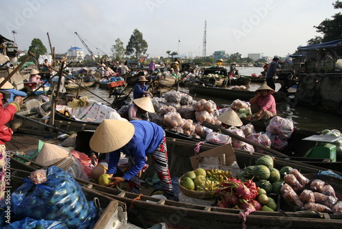 Mercado flotante de Cai Rang, Vietnam, delta del Mekong, muchas pequeñas barcas con frutas y verduras venden apiñadas la mercancía con compradores con gorros típicos  photo