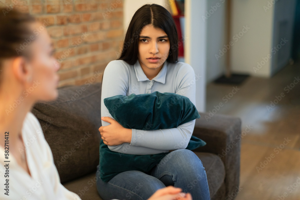 Mother having serious conversation with her teen daughter, sitting together on sofa, lady hugging pillow, looking at mom - obrazy, fototapety, plakaty 