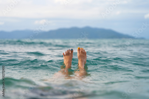 Wall Mural A girl with a yellow and blue pedicure relaxes in the sea overlooking the island