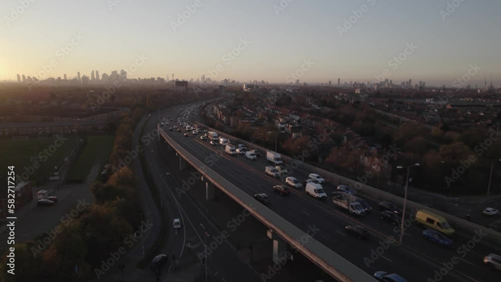 Long queue of slowly moving vehicles on multilane trunk exit road from city. Silhouette of downtown skyscrapers against sunset sky. London, UK Long queue of slowly moving vehicles on multilane trunk exit road from city. Silhouette of downtown skyscrapers against sunset sky. London, UK