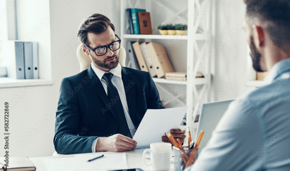 Confident HR manager examining CV while interviewing job candidate in the office