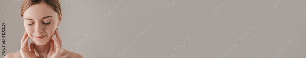 Portrait of freckled redhead woman touching face against grey background Portrait of freckled redhead woman touching face against grey background