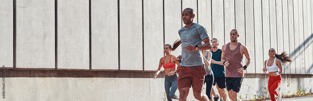 © gstockstudio - Group of confident young people in sports clothing jogging outdoors together