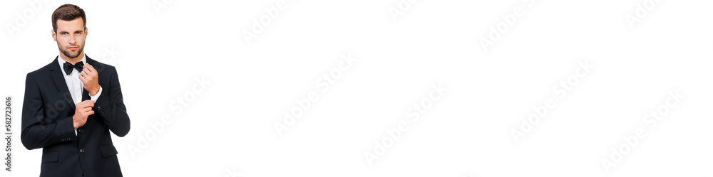 Handsome young man in suit and bow tie adjusting his sleeve against white background Handsome young man in suit and bow tie adjusting his sleeve against white background