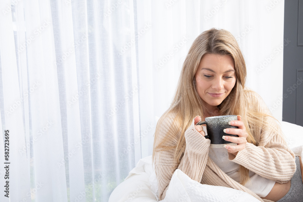 Young lady drinking hot drink in white bed relaxing Young lady drinking hot drink in white bed relaxing