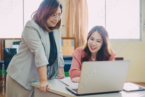 Two professional business women having a discussion in a startup. Cheerful business people using a laptop in office working together on a creative project.