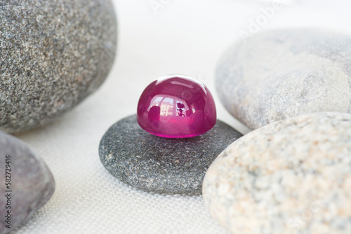 Natural red ruby cabochon drop shaped gestone loose polished translucent setting lying on a gray flat pebble stone. Pebbles around on white fabric background. Gemology, mineralogy, nature theme. photo