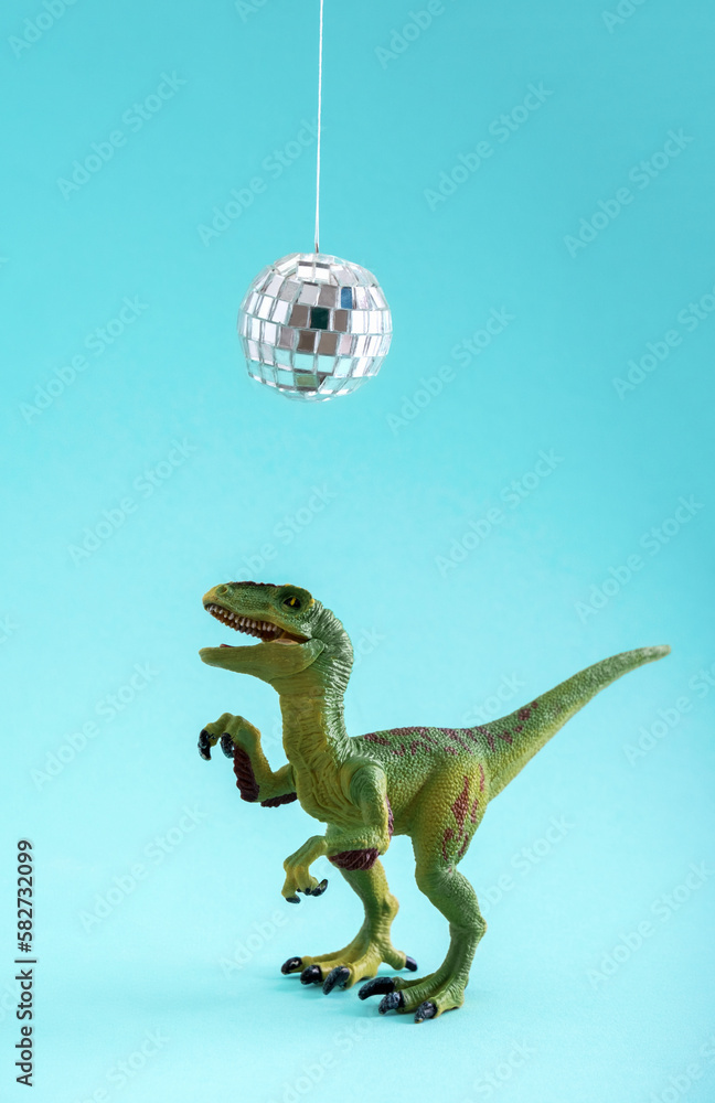 Obraz premium Happy cute green toy dinosaur dancing under disco ball on blue background. Minimal creative art poster.