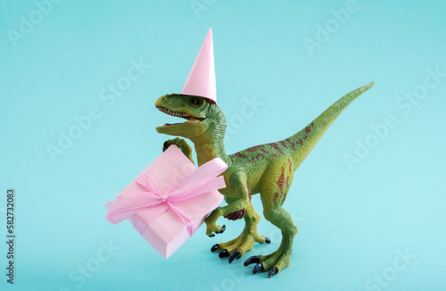 Cute green dinosaur with gift box and party hat on a blue background. Cute minimal birthday concept. © dvulikaia