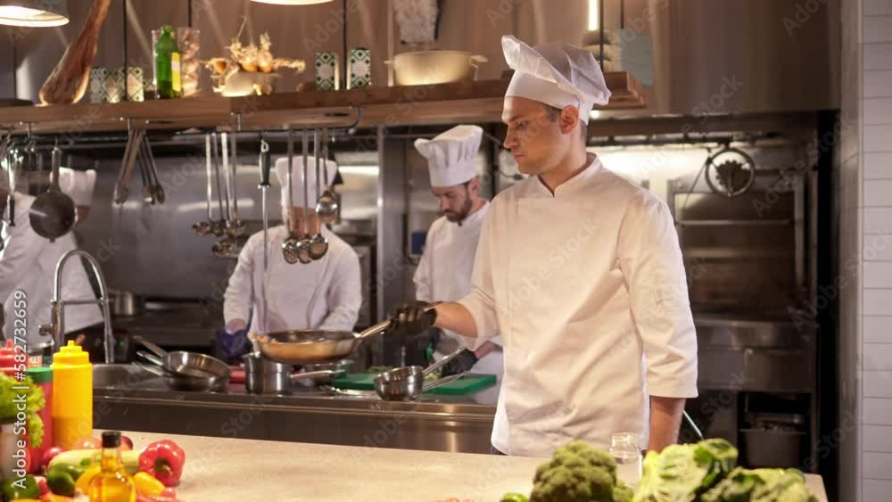 Side-view portrait of skillful professional caucasian male cook holding pan frying and mixing delicious food. Handsome young experienced chef in white uniform cooking in modern kitchen. Side-view portrait of skillful professional caucasian male cook holding pan frying and mixing delicious food. Handsome young experienced chef in white uniform cooking in modern kitchen.