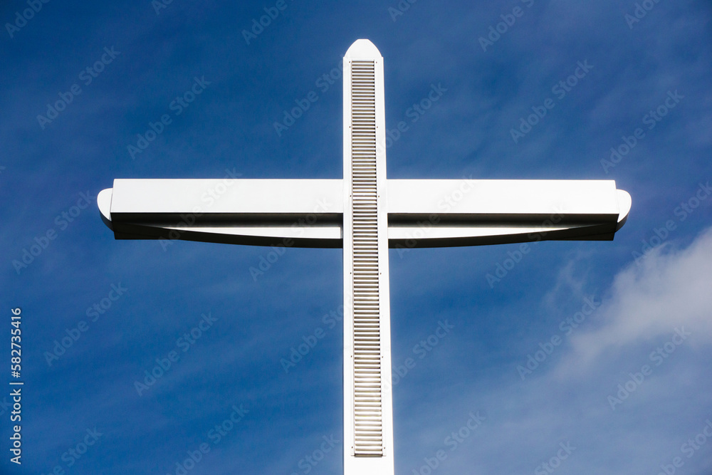 Big metal christian cross high in the blue sky. Symbol of love for Jesus. Catholic church monumental construction. Crucified jesus christ. Outdoor pray.