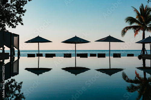 Reflection of beach umbrellas on pool surface in front of an ocean just after sunset © Felix Haumann
