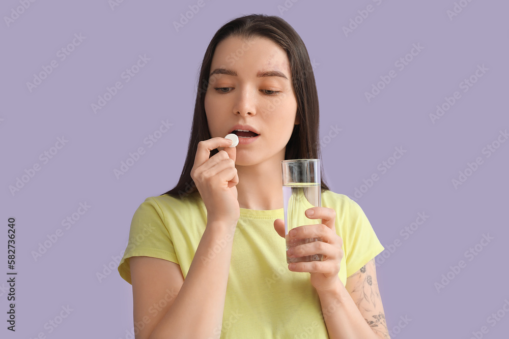 Young woman with glass of water taking vitamin supplement on lilac background Young woman with glass of water taking vitamin supplement on lilac background
