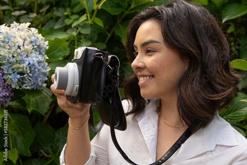 Mulher sorrindo em um dia ensolarado enquanto tira fotos na natureza com uma câmera instanânea photo