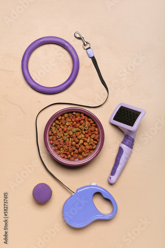Bowl of dry pet food, toys, grooming brush and leash on color background