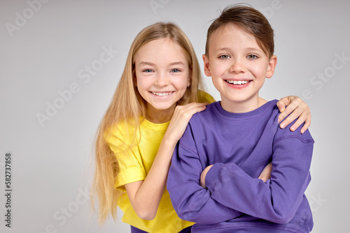 Happy kids are standing together at sudio. close up portrait, friendly brother and sidter look at camera, blonde happy girl hugs, puts her arms on her boyfriend shoulder photo