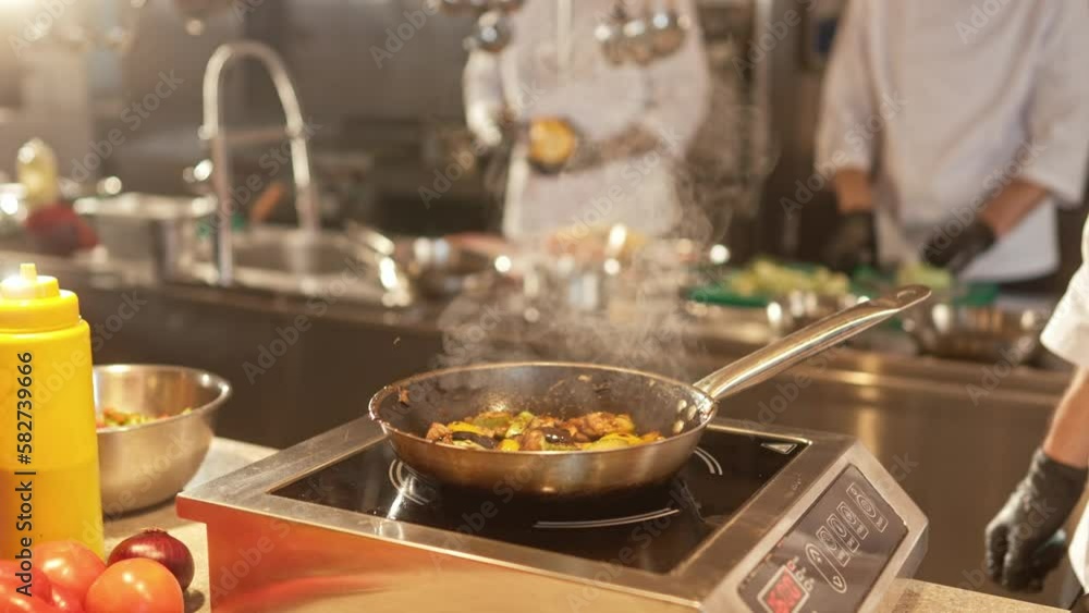 Close-up view of tasty vegetables being fried on pan by young caucasian professional chef in white uniform and black gloves at modern restaurant kitchen. Cooking concept, Close-up view of tasty vegetables being fried on pan by young caucasian professional chef in white uniform and black gloves at modern restaurant kitchen. Cooking concept,