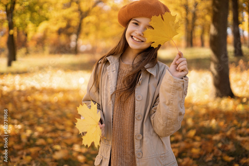 Excited happy fall girl smiling joyful holding autumn leaves outside in colorful fall forest. Autumn portrait of teen girl with yellow maple leaves