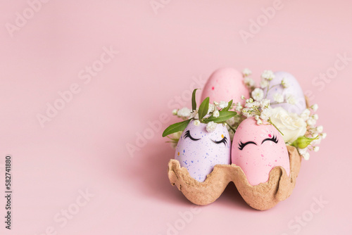 Banner. Stylish Easter pink and liliac eggs with cute faces in floral wreath crowns in carton tray on pink background. Easter decorations and gift. Happy Easter concept. Copy space. Isolated.